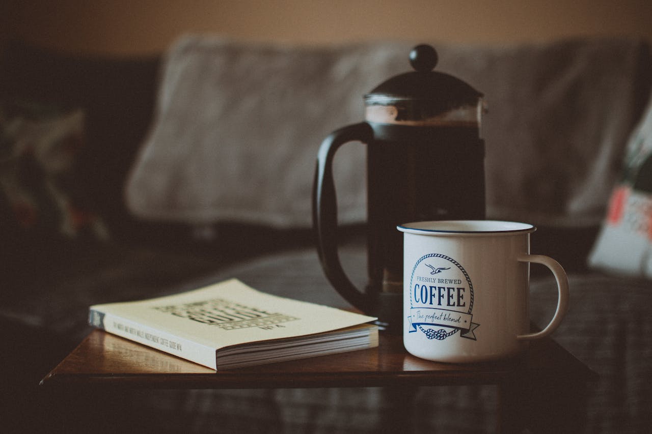 services-01 A warm setting with a coffee cup, book, and French press on a table.