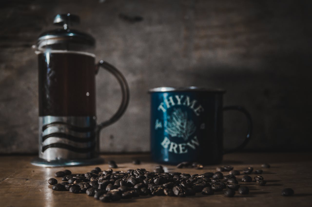 A cozy scene featuring a French press, a mug labeled 'Thyme for Brew', and coffee beans on a wooden table.