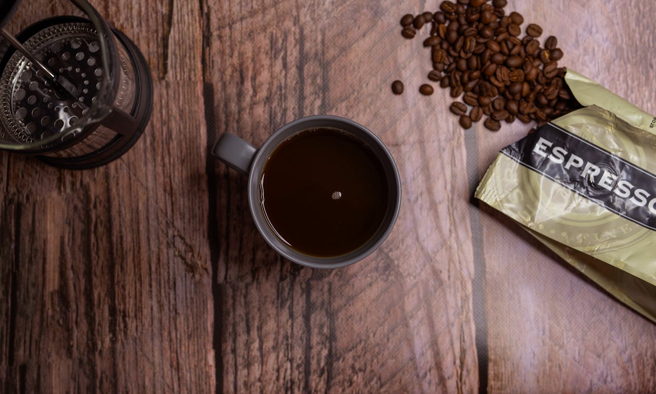 Top-down view of a coffee cup, French press, and espresso beans on a rustic wooden surface.