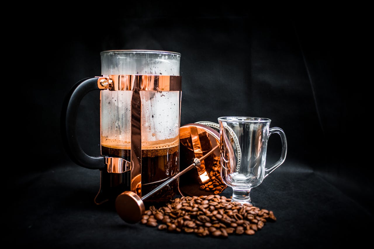 Stylish French press with glass cup, surrounded by coffee beans, perfect for brewing enthusiasts.