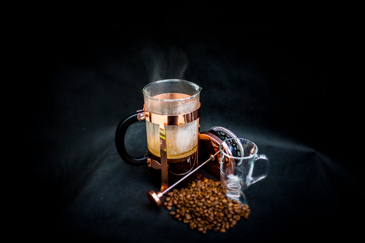 Stylish French press with steaming coffee and beans on black background.